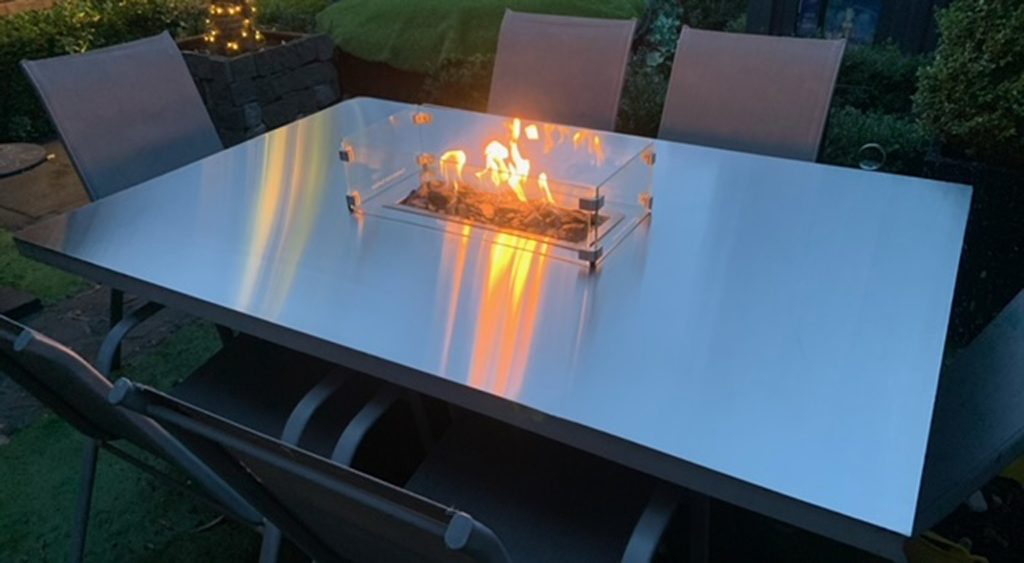 Brushed stainless steel table top with a floating fire pit lit up at night